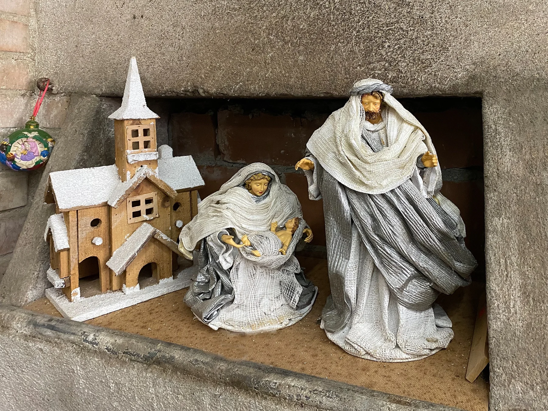 Krippenfiguren neben einer kleinen Kirche in winterlicher Kulisse