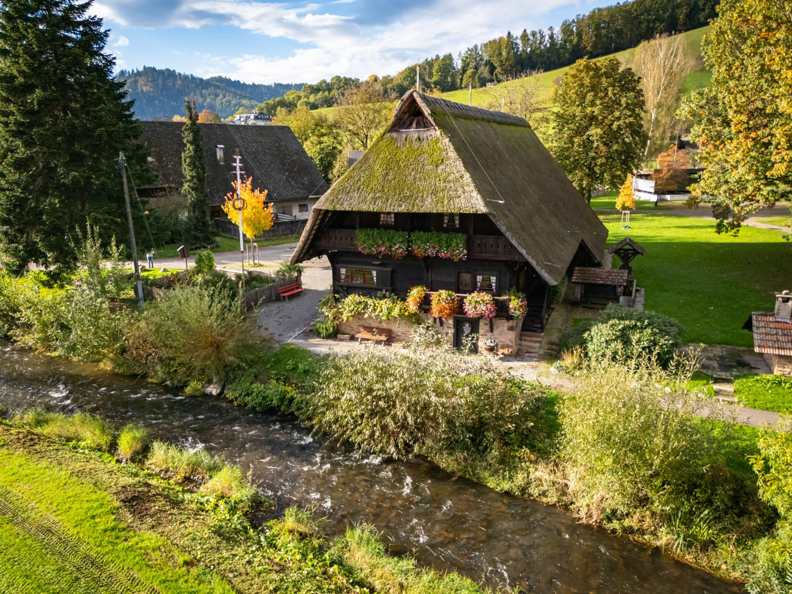 Fürstenberger Hof mit strohgedecktem Dach, Blumen und grünen Wiesen am Bach